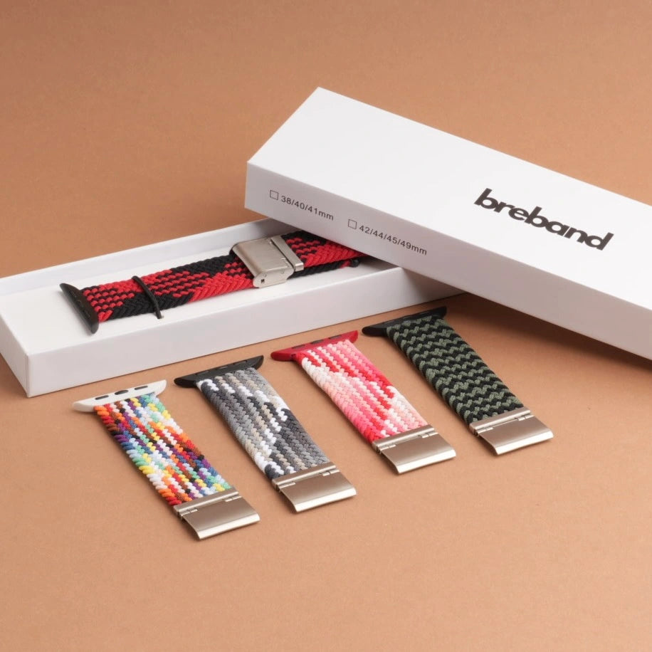 Geflochtene Nylonarmbänder für Apple Watch in verschiedenen Farben präsentiert vor Breband Verpackungen in stilvoller Anordnung.