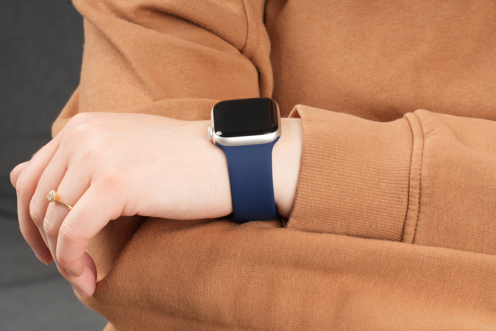 Apple Watch mit dunkelblauem Silikonarmband am Handgelenk getragen über einem braunen Pullover.