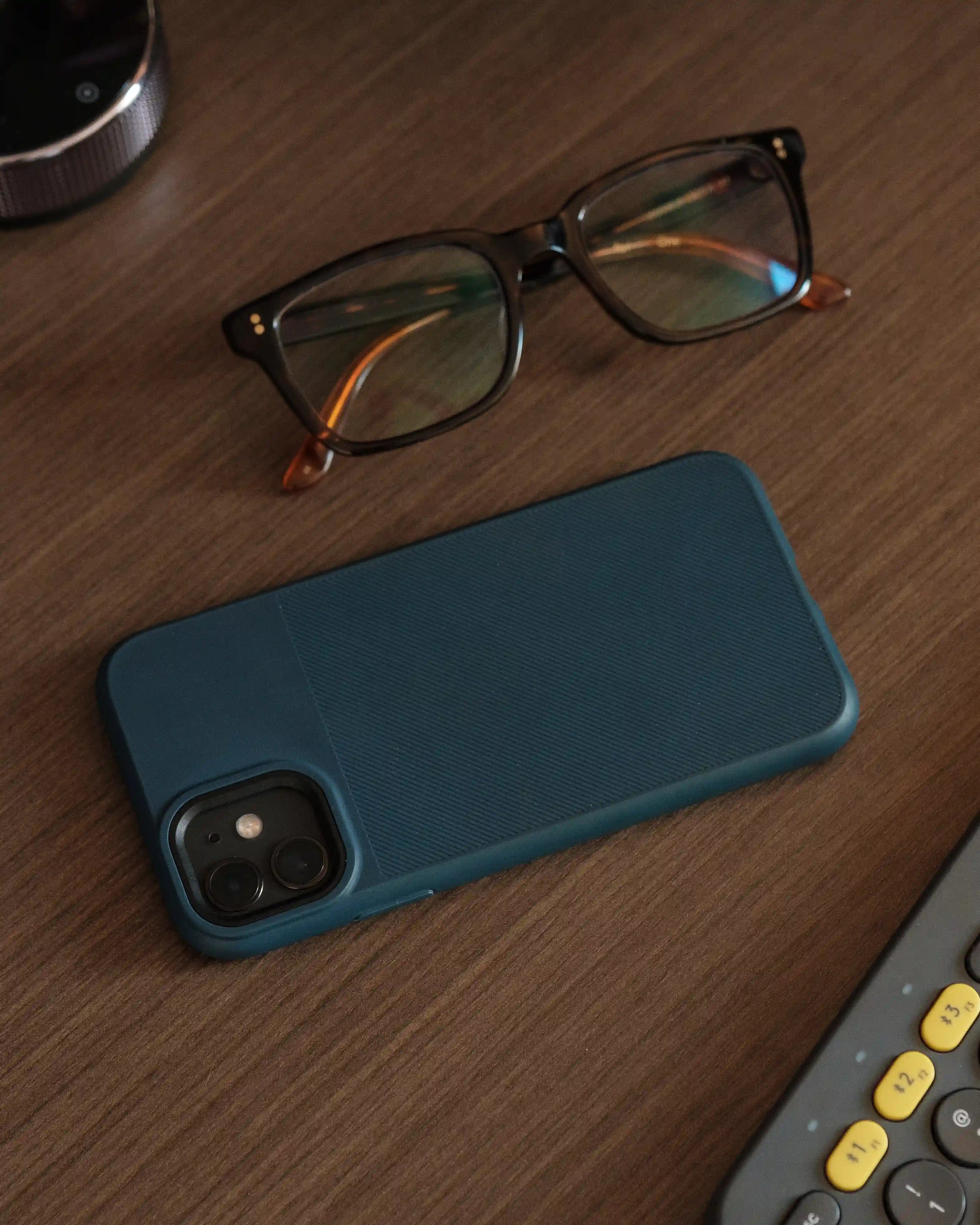 Dunkelblaue iPhone Silikon Handyhülle auf einem Holztisch neben einer Brille