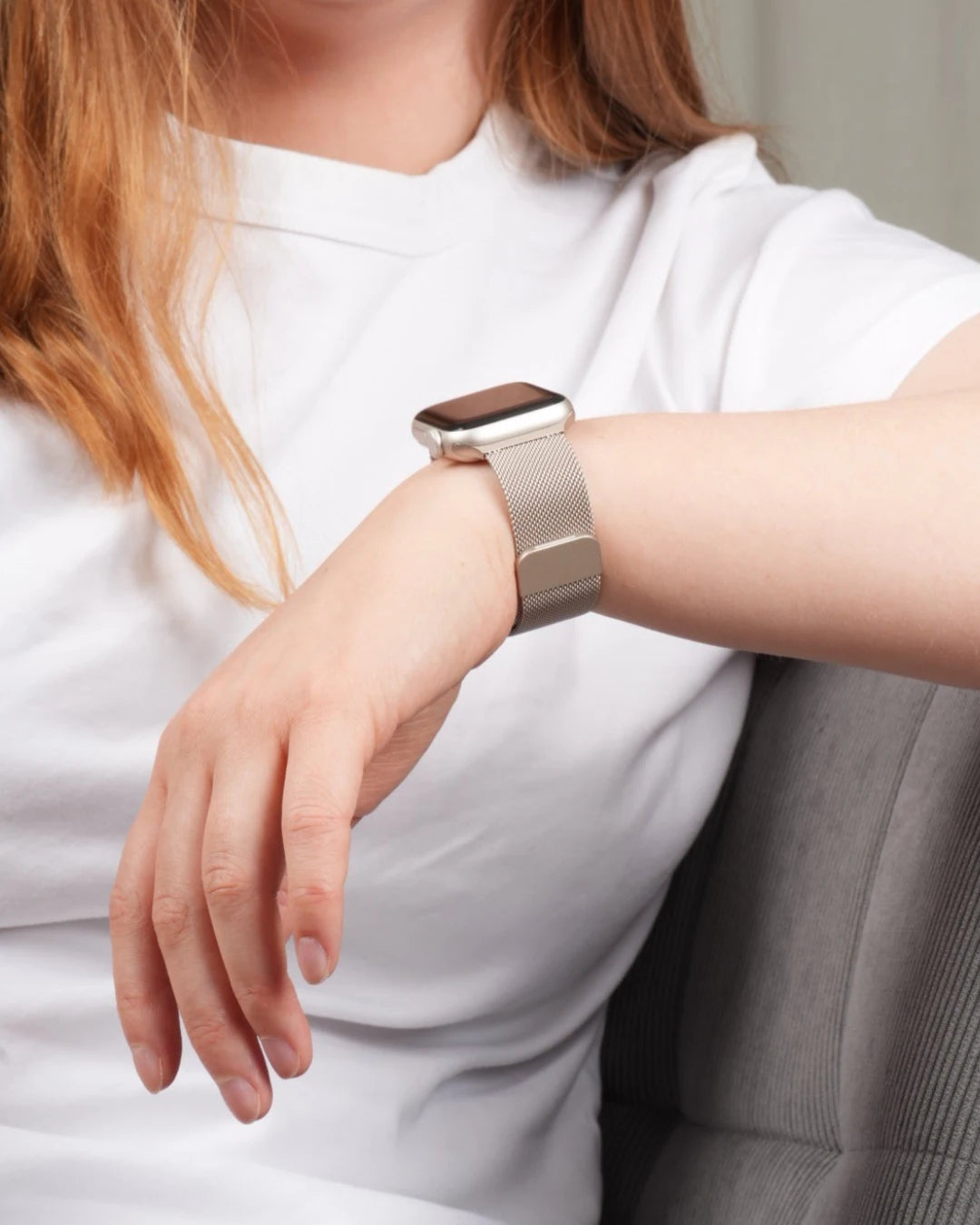 Apple Watch mit silbernem Milanaise-Armband am Handgelenk einer sitzenden Person mit weißem T-Shirt