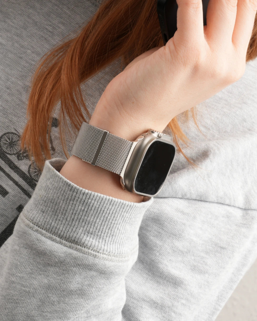 Apple Watch mit silberfarbenem Milanaise Armband am Handgelenk einer Person im grauen Sweatshirt