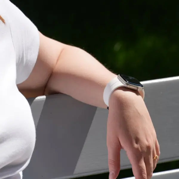 Apple Watch mit weißem Silikonarmband am Handgelenk einer Person im Freien auf einer Bank