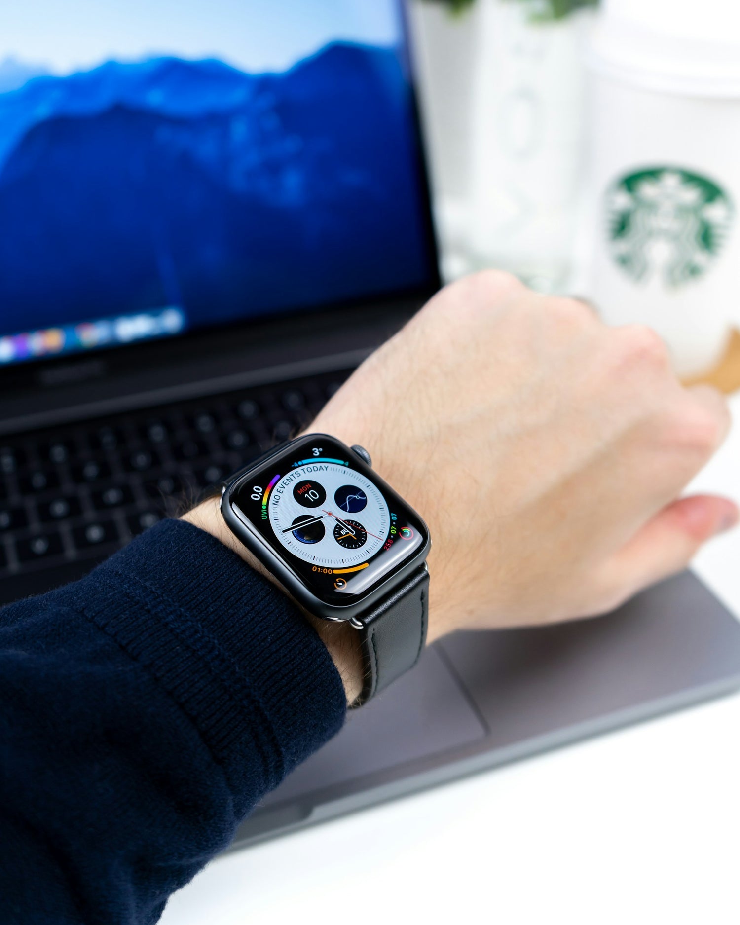 Apple Watch mit schwarzem Lederarmband am Handgelenk vor einem Laptop