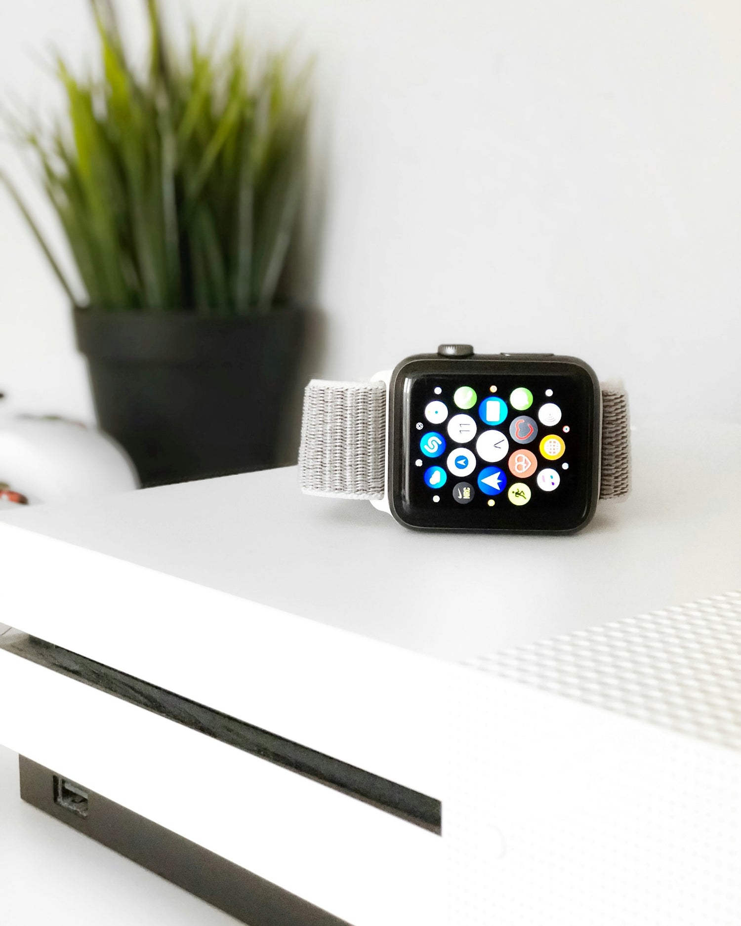 Apple Watch mit grauem Stoffarmband, abgelegt auf einem weißen Tisch.