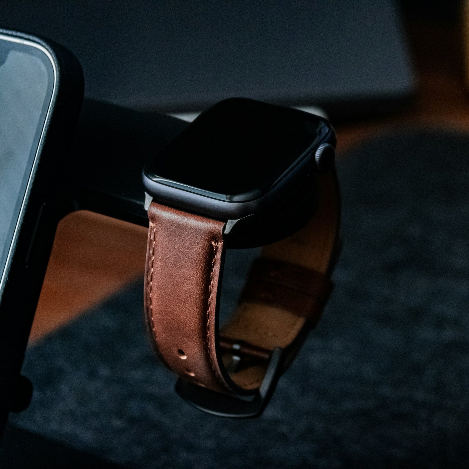 Apple Watch mit braunem Lederarmband auf einer Ladestation in einer dunklen Umgebung.